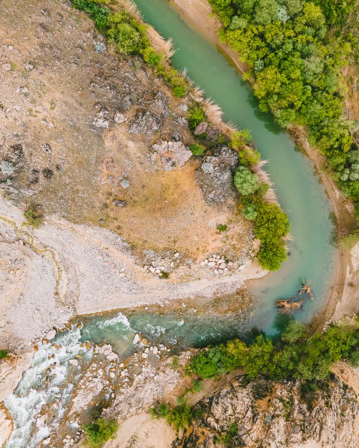 private-party-02 Aerial shot of a winding river cutting through a mountainous terrain with lush vegetation.