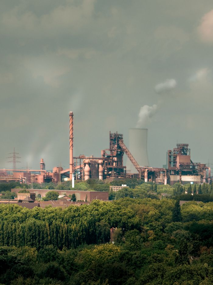 View of a sprawling industrial plant emitting smoke, surrounded by greenery in Duisburg.