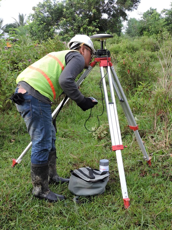testimonial-image A surveyor using equipment in lush Indonesian terrain, wearing safety gear.
